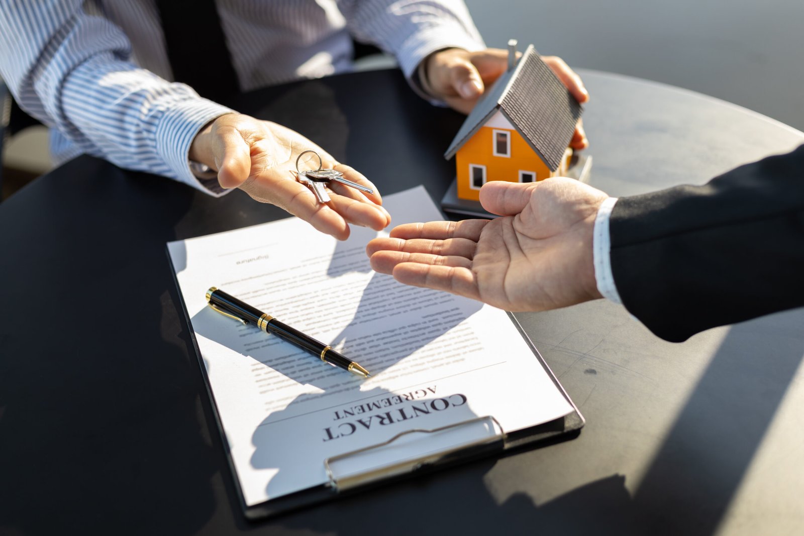 Real estate agent handing home keys to client after signing home purchase agreement. Signing real estate agreements, buying-selling, renting and mortgages.